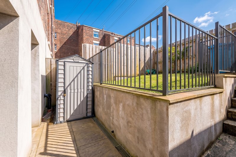 Exterior patio with metal railings, shed, and brick residential buildings beyond