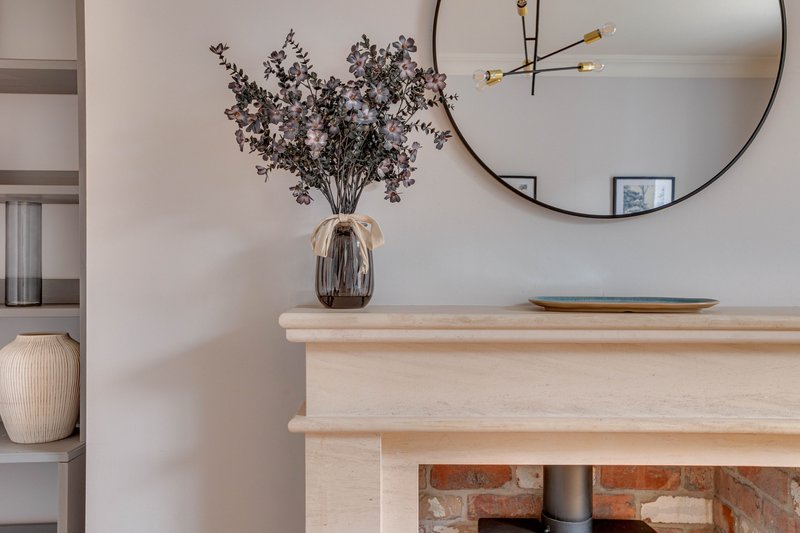 Fireplace mantel with dried flowers in vase, round mirror and pendant light fixture