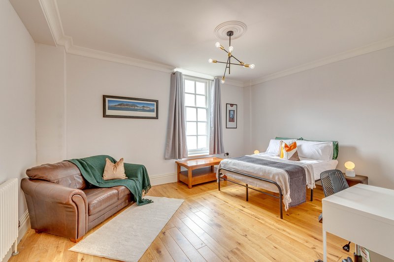 Bright bedroom with brown leather sofa, single bed, wooden floor and large window