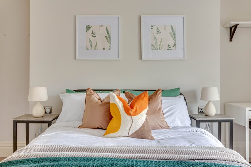Bedroom with double bed, colorful cushions, framed botanical art, and bedside tables with lamps