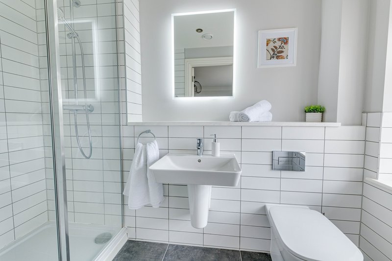 Modern bathroom with white subway tiles, illuminated mirror, pedestal sink and shower enclosure