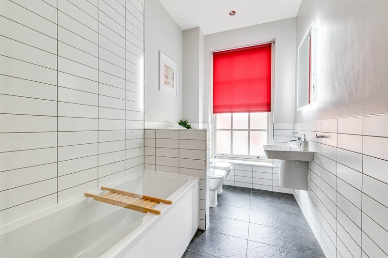 Modern bathroom with white subway tile walls, bathtub, sink, and red window blind