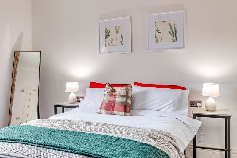 Bedroom with double bed, red headboard, turquoise throw, white bedding and botanical wall art
