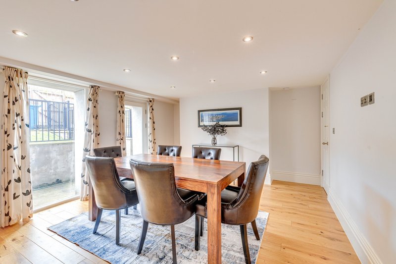 Bright dining room with wooden table, upholstered chairs, blue rug, and garden doors
