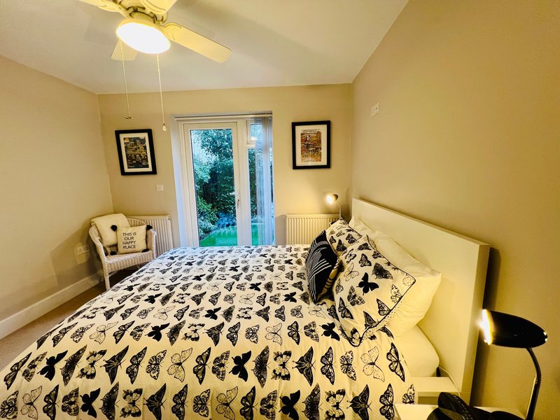 Bright yellow bedroom with double bed, patterned bedding, framed wall art, and glass doors to garden