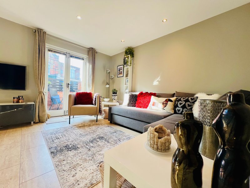 Modern living room with sofa, armchair, TV, rug and large windows with garden view