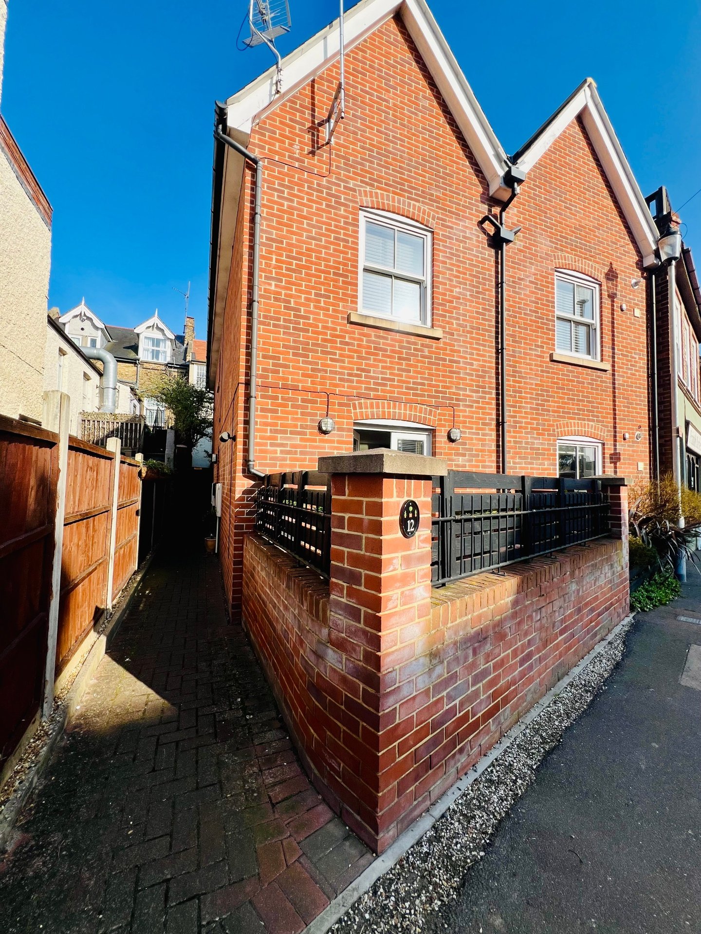 Red brick detached house exterior with driveway, black gate and clear sky