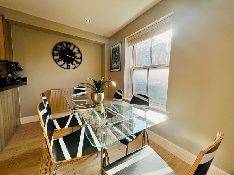 Modern dining area with glass table, patterned chairs, wall clock and large windows