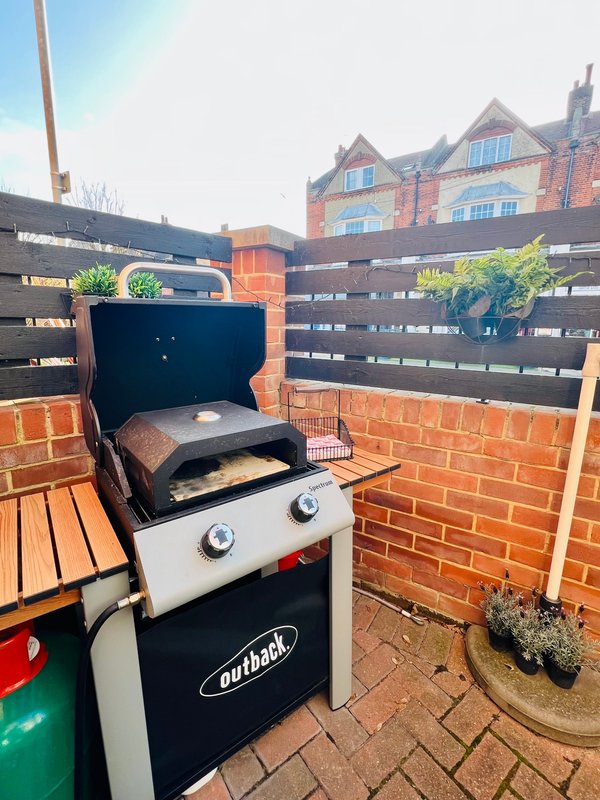 Outdoor patio area with gas barbecue grill, wooden furniture and brick walls