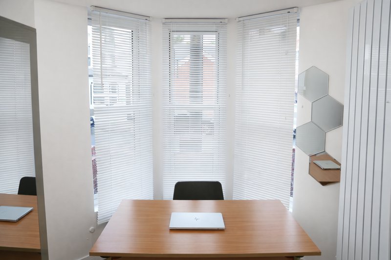 Small office room with wooden desk, black chairs, and hexagonal wall shelving