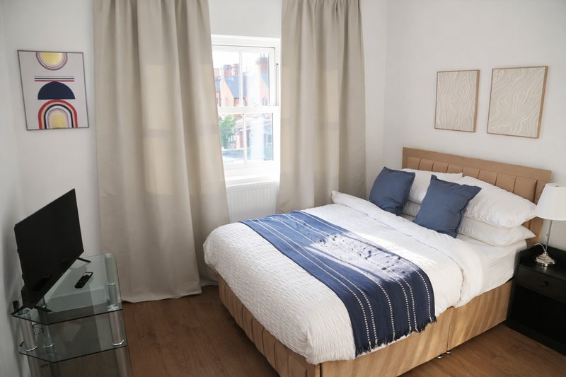 Bright bedroom with double bed, wooden headboard, blue pillows, and window with city view
