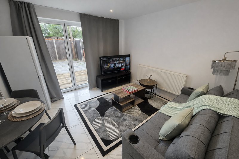 Open-plan living room with grey sofa, TV, dining area, and patio doors overlooking garden