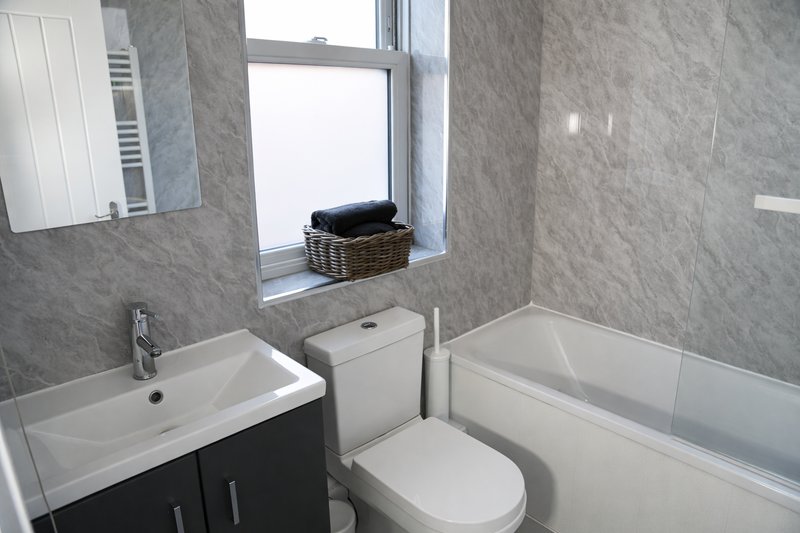 Modern bathroom with sink vanity, toilet, bathtub and window with gray tile walls