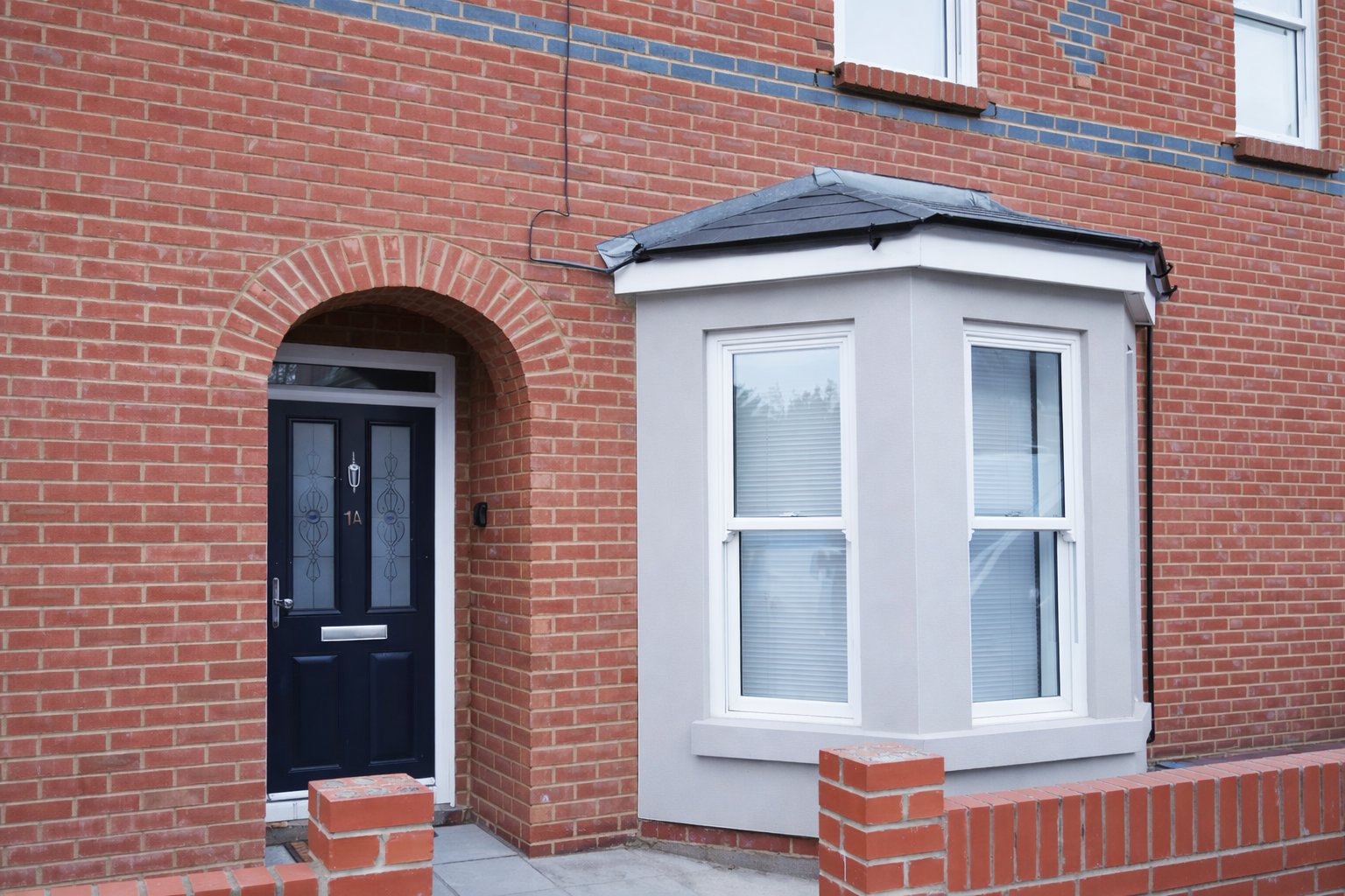 Red brick terraced house exterior with black door and white bay window