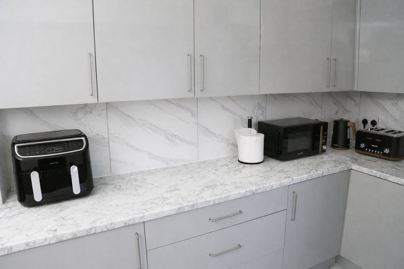 Modern kitchen with white cabinetry, marble countertop and black appliances