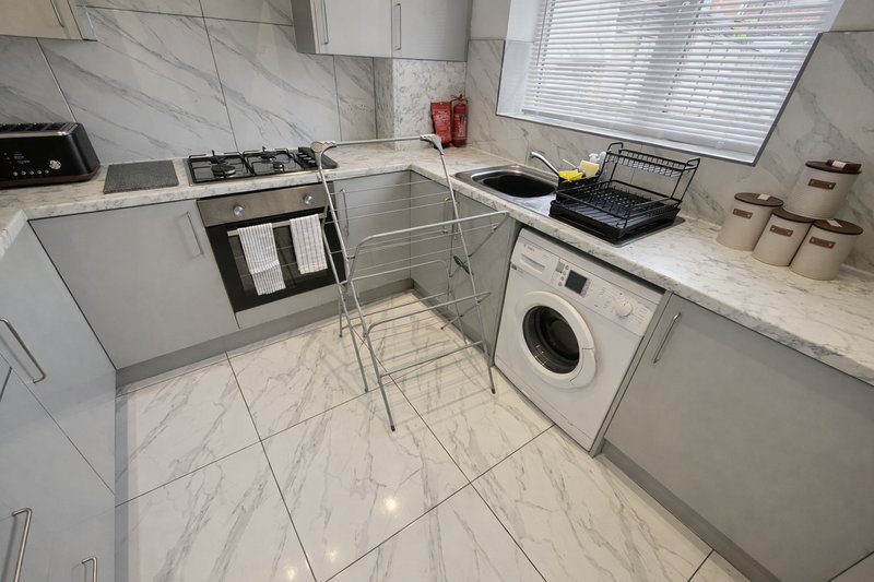 Modern kitchen with white cabinets, marble countertops, gas range and washing machine