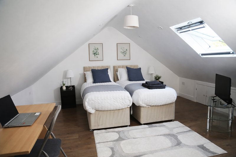 Modern attic bedroom with two beds, wooden desk, pendant light and skylight window