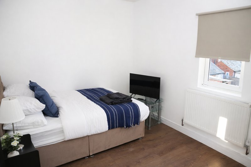 Bright bedroom with double bed, navy bedding, small TV, and window with blind