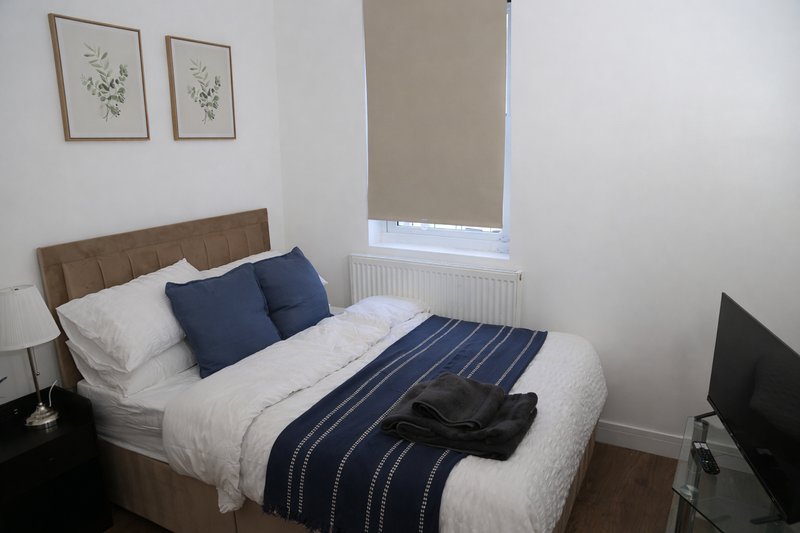 Bedroom with double bed, navy bedding, upholstered headboard, and framed botanical prints