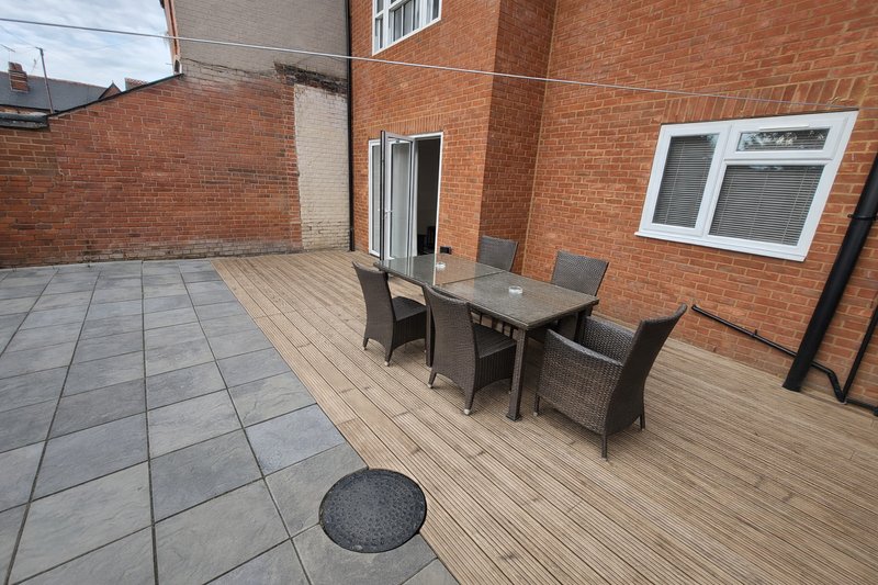 Outdoor patio with dining table, chairs, brick building and wooden decking