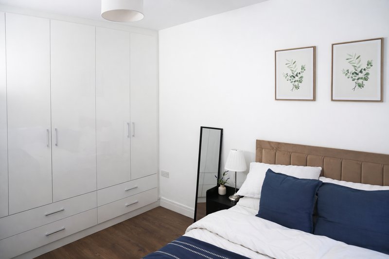 Modern bedroom with double bed, white fitted wardrobes, dark wood flooring and botanical wall art