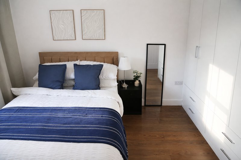 Bright bedroom with double bed, blue bedding, tan headboard, wooden floor and minimal decor
