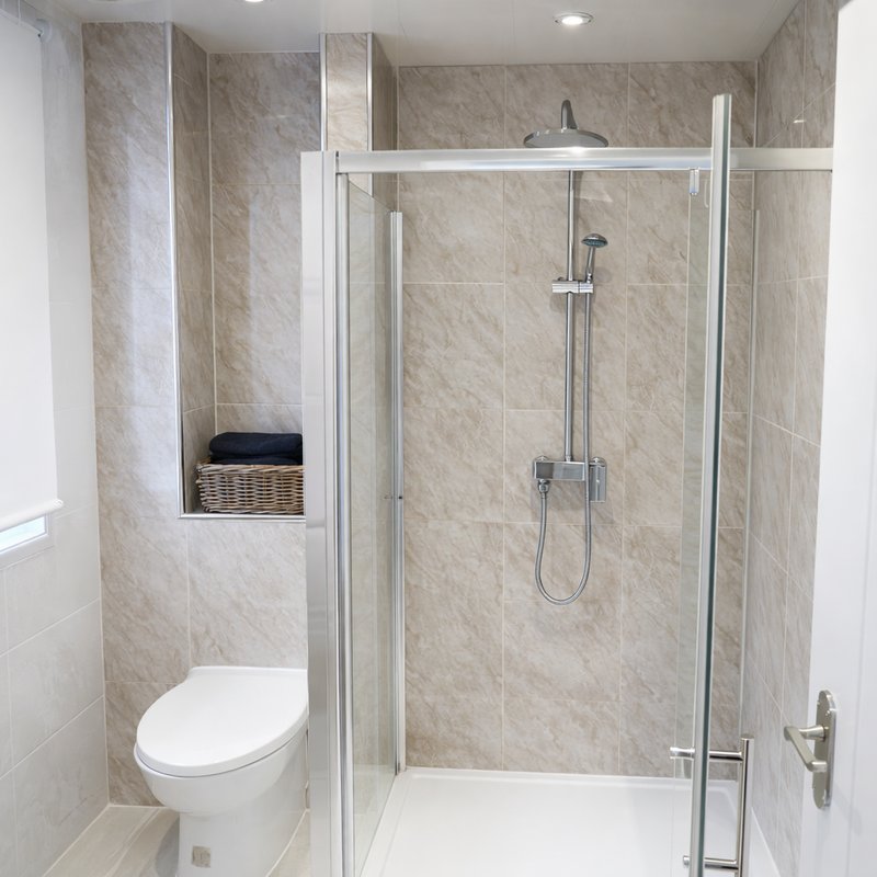 Modern bathroom with walk-in shower, toilet, and beige tile walls throughout