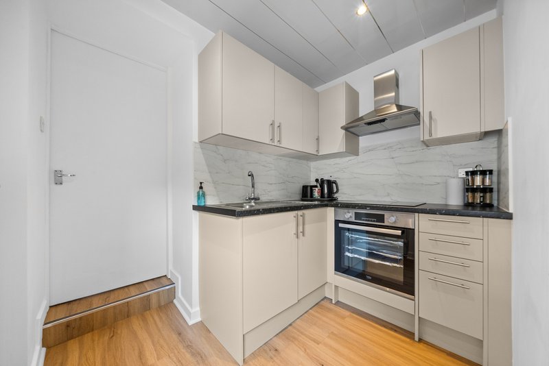 Modern kitchen with cream cabinets, black countertops, stainless steel appliances and wooden flooring