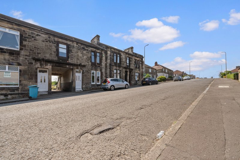 Street-facing stone terraced houses with parked car and clear sky