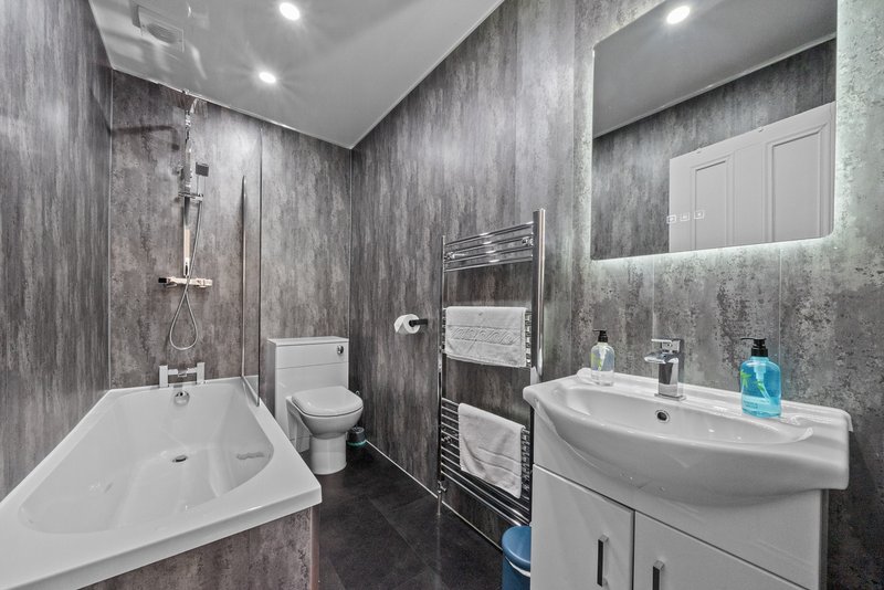 Modern bathroom with bathtub, toilet, sink vanity, heated towel rail and grey tile walls
