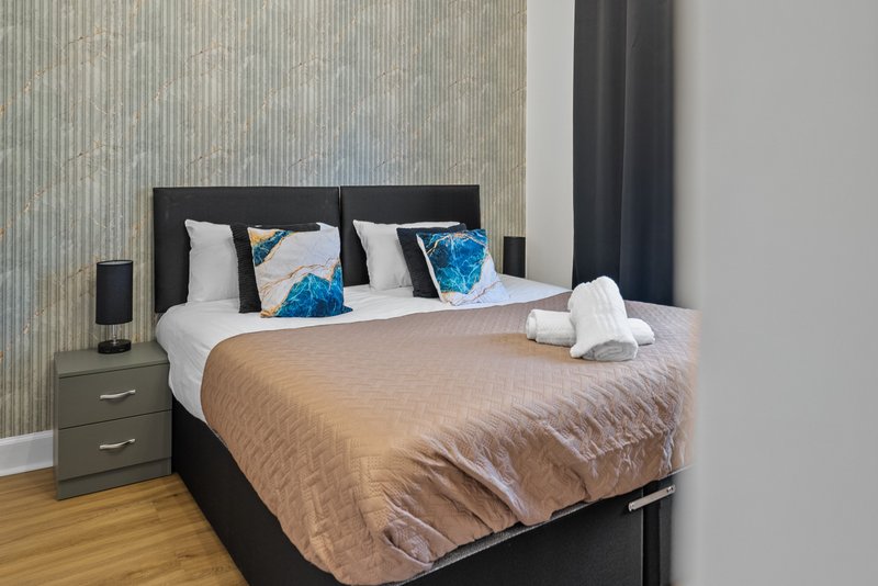 Modern bedroom with black bed frame, beige bedding, blue decorative pillows and wooden flooring