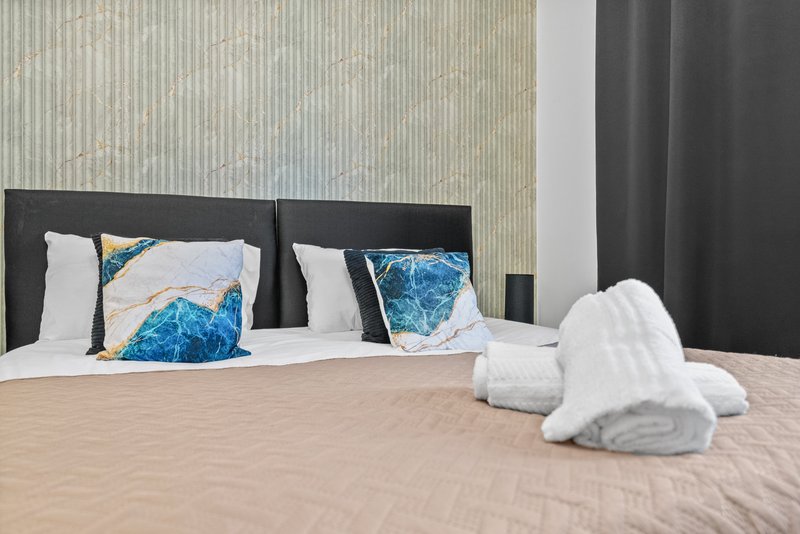 Modern bedroom with double bed, decorative pillows, white towels and dark headboard