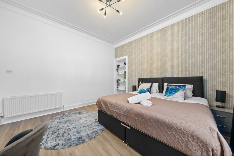 Spacious bedroom with double bed, wooden flooring, textured accent wall and modern ceiling light