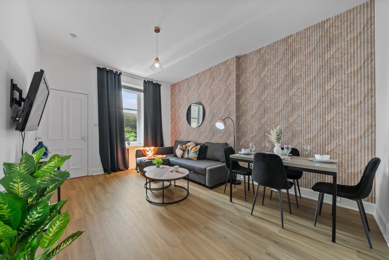Modern living room with black sofa, dining table, wood flooring, and brick accent wall