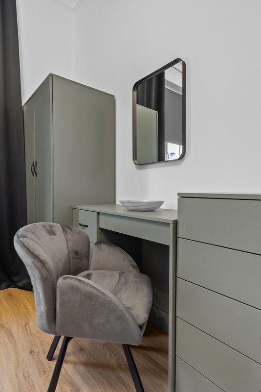 Bedroom dressing area with sage green desk, upholstered chair, and wall-mounted mirror