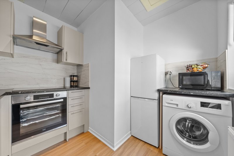 Modern kitchen with cream cabinets, built-in oven, white fridge-freezer, washing machine and wooden flooring