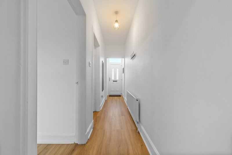 Long narrow hallway with white walls, wooden flooring, ceiling lights and multiple doors