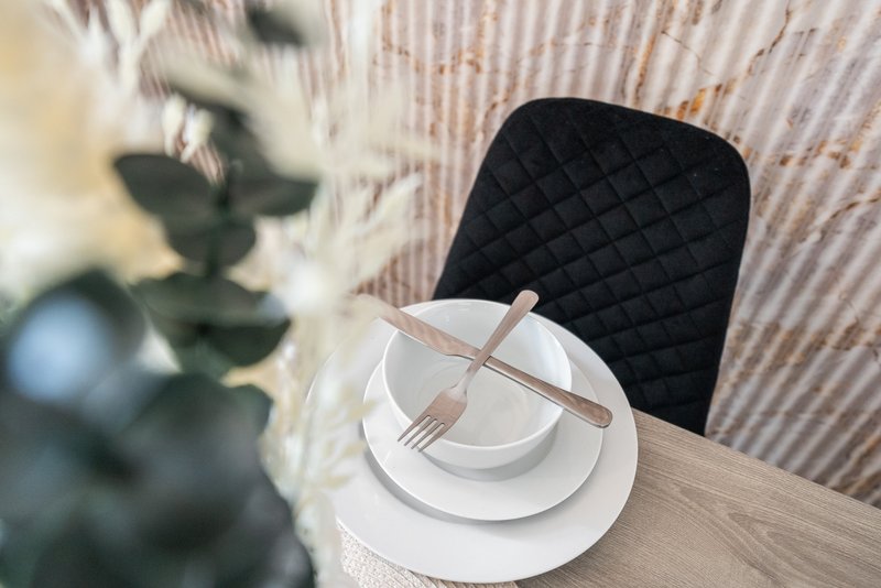 Dining table with place setting, black chair, and potted plant in background