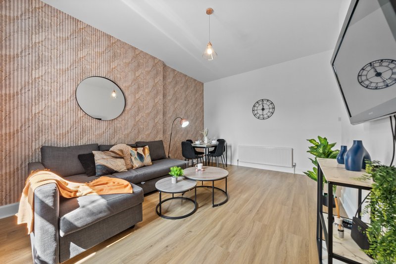 Modern living room with gray sofa, wooden accent wall, round mirror, and wooden flooring