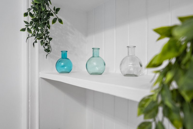 White shelf with three decorative glass bottles and hanging green plants