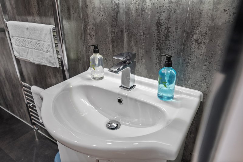 Modern bathroom sink with chrome tap, clear glass and blue toiletries bottle