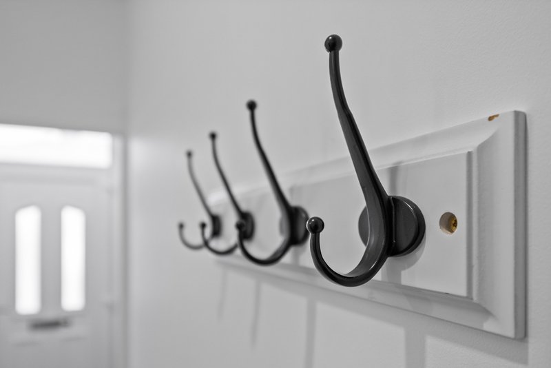 White wall-mounted coat rack with four black hooks and brass detail