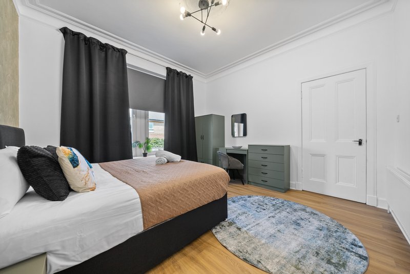 Bedroom with double bed, black frame, patterned rug, dark curtains and wooden floor