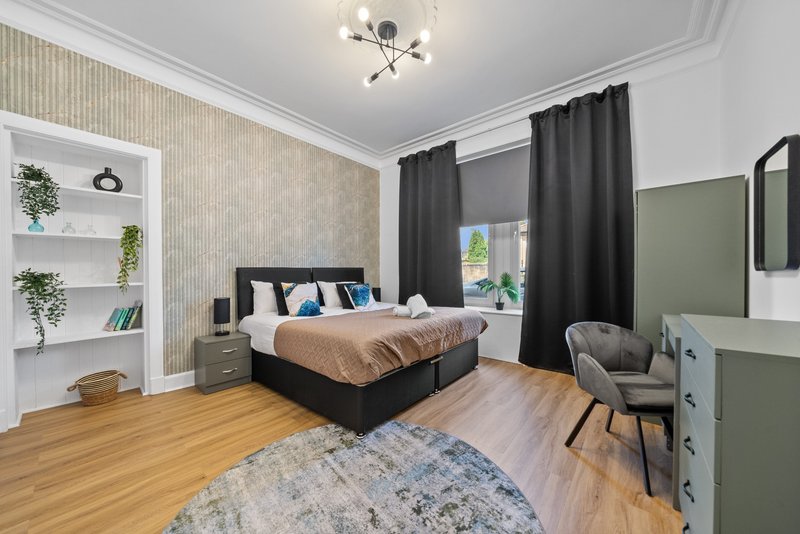 Modern bedroom with black bed, wooden flooring, green accent wall and white shelving