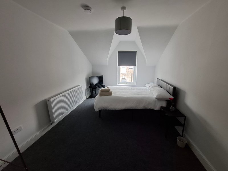 Minimal bedroom with white walls, black floor, single bed and pendant lamp