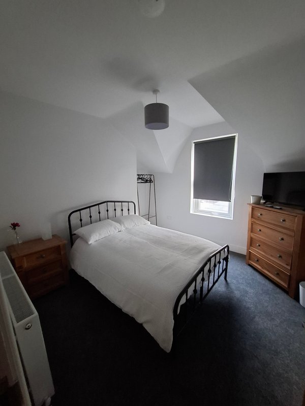 Bedroom with single bed, wooden dresser, nightstand, pendant light and window