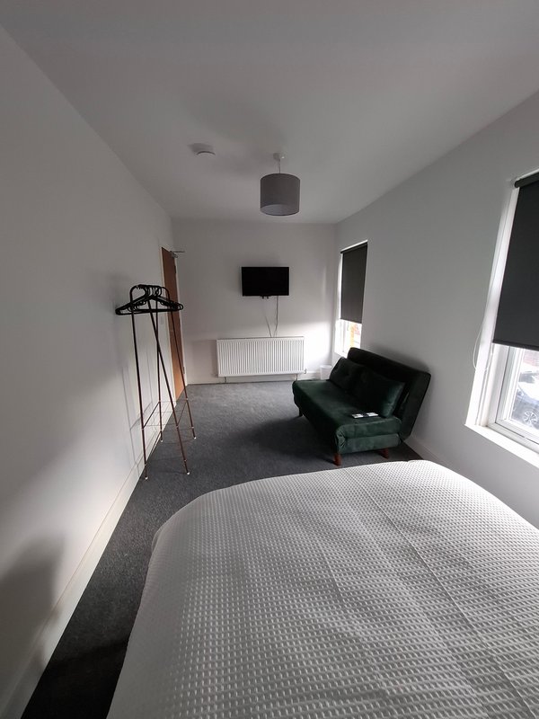Modern bedroom with bed, green armchair, wall-mounted TV, and natural light from windows