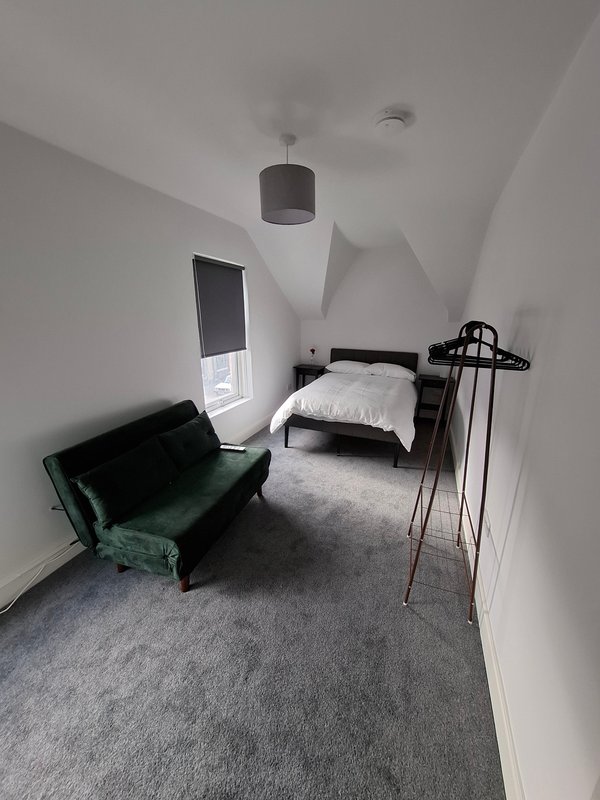Modern attic bedroom with single bed, green sofa, grey carpet and skylight window