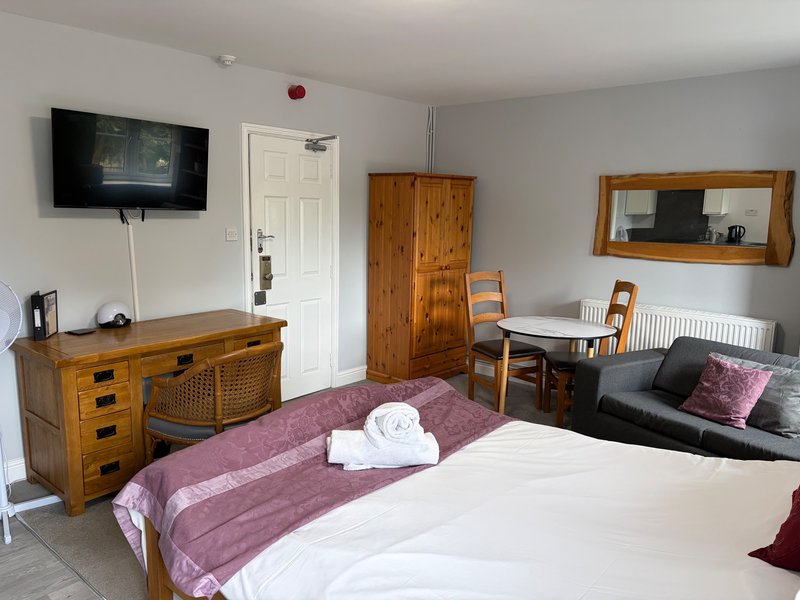 Spacious bedroom with double bed, wooden furniture, TV, dining table and seating area