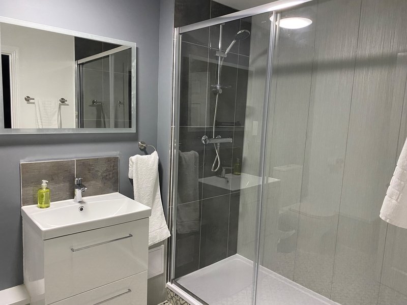 Modern bathroom with white vanity, mirror, sink, and glass-enclosed shower cubicle